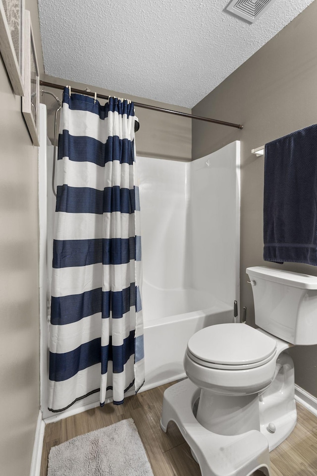 bathroom with shower / bath combo with shower curtain, a textured ceiling, toilet, and wood finished floors