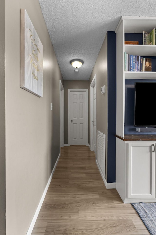 hall featuring a textured ceiling, light wood-type flooring, visible vents, and baseboards