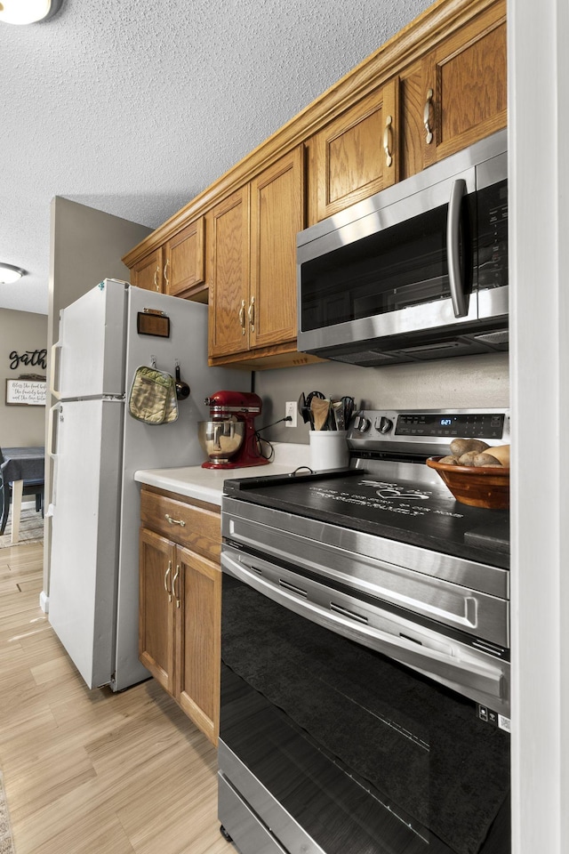 kitchen with brown cabinetry, appliances with stainless steel finishes, light countertops, a textured ceiling, and light wood-style floors