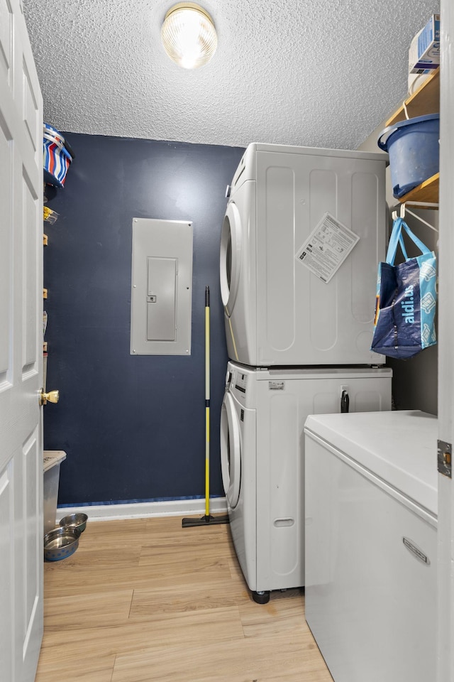 laundry area featuring laundry area, electric panel, stacked washer and clothes dryer, light wood-style flooring, and a textured ceiling