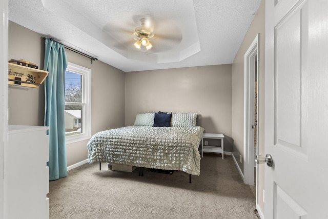 carpeted bedroom with ceiling fan, baseboards, a raised ceiling, and a textured ceiling