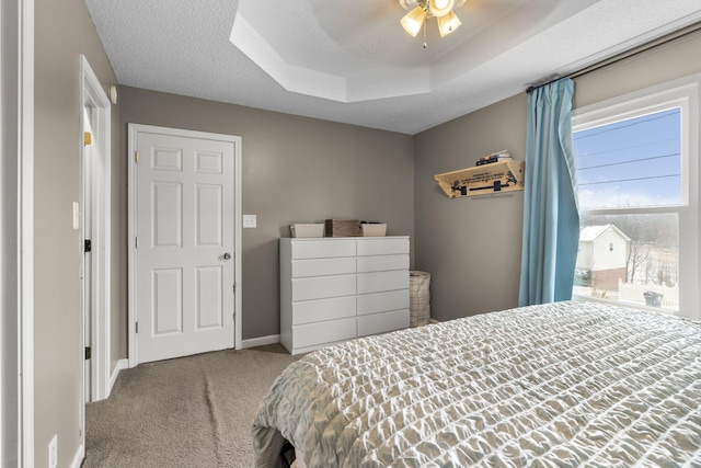 bedroom with a textured ceiling, light carpet, a ceiling fan, baseboards, and a tray ceiling