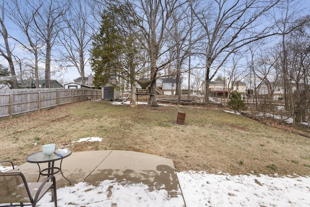 yard covered in snow with a fenced backyard, an outdoor structure, a patio, and a shed