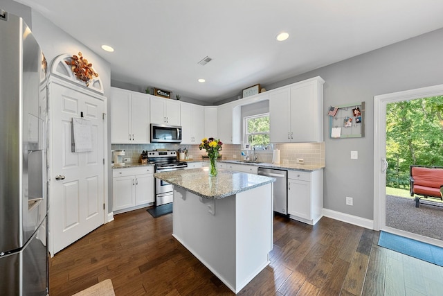 kitchen with white cabinets, appliances with stainless steel finishes, light stone counters, dark wood-type flooring, and a center island