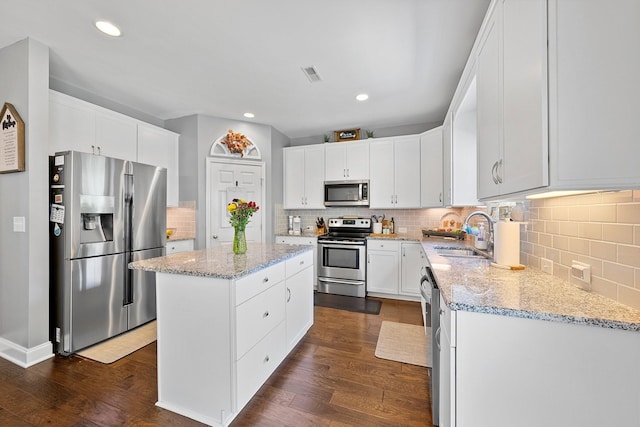 kitchen with stainless steel appliances, light stone countertops, a sink, and a kitchen island