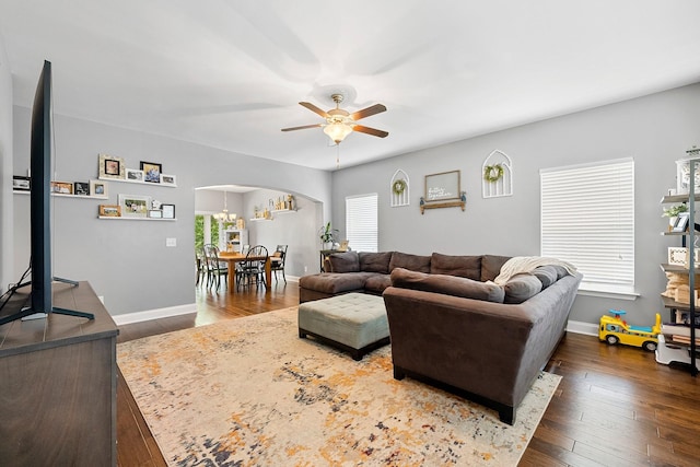 living area featuring arched walkways, dark wood finished floors, baseboards, and ceiling fan