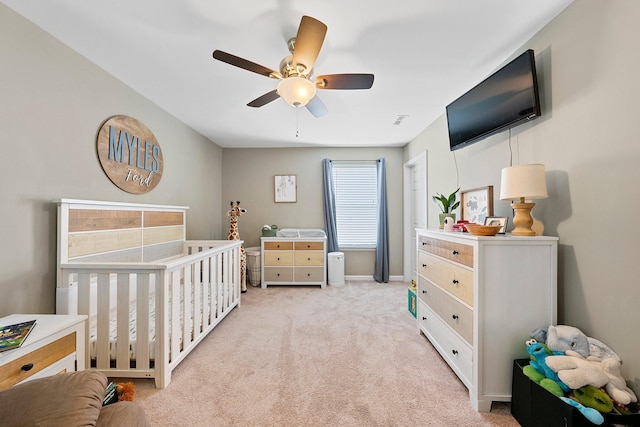 bedroom with a nursery area, ceiling fan, baseboards, and light colored carpet