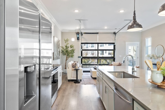 kitchen with appliances with stainless steel finishes, decorative light fixtures, crown molding, light wood-style floors, and a sink