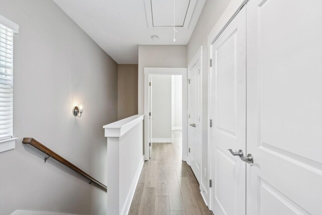 hallway with attic access, baseboards, light wood-style flooring, and an upstairs landing