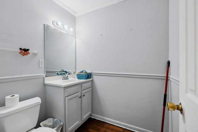 bathroom featuring baseboards, toilet, ornamental molding, wood finished floors, and vanity