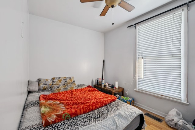 bedroom featuring ceiling fan, wood finished floors, visible vents, and baseboards