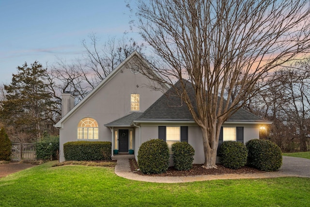 view of front of home featuring roof with shingles, a lawn, fence, and stucco siding