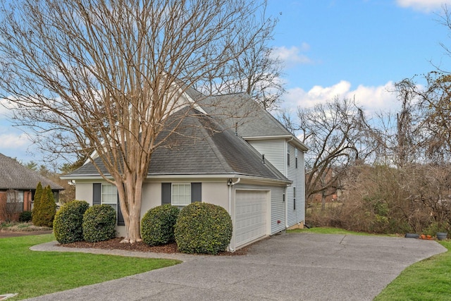 view of side of property featuring a shingled roof, aphalt driveway, an attached garage, a yard, and stucco siding