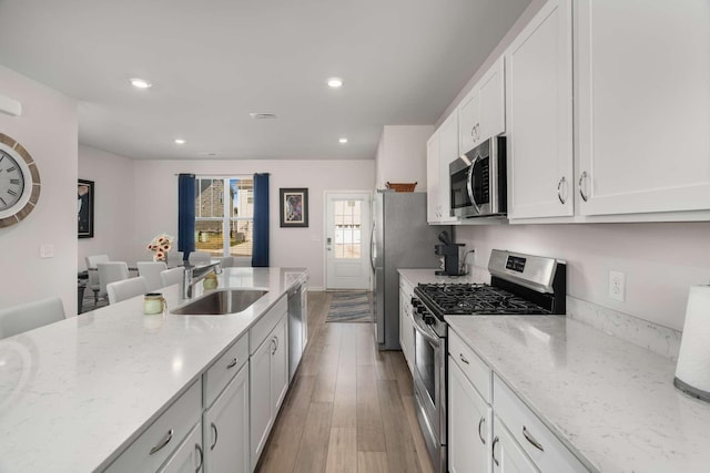 kitchen featuring light stone counters, appliances with stainless steel finishes, white cabinetry, a sink, and wood finished floors