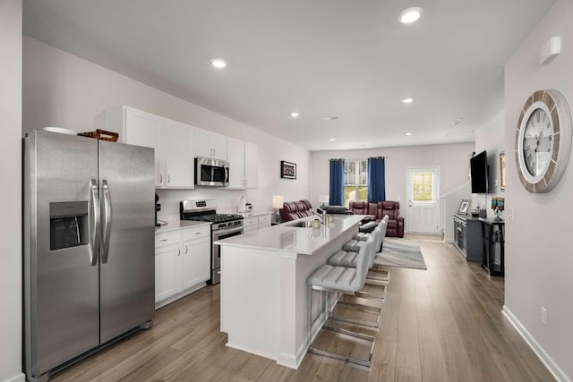 kitchen featuring stainless steel appliances, open floor plan, white cabinetry, a sink, and wood finished floors