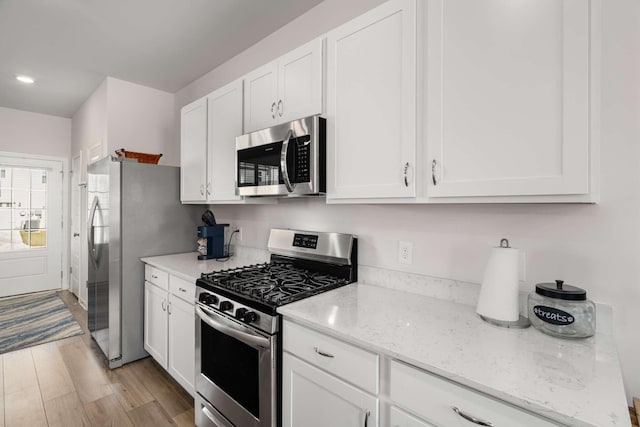 kitchen featuring appliances with stainless steel finishes, white cabinets, light wood-style flooring, and light stone counters