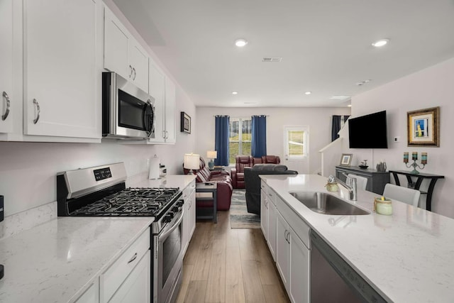 kitchen with visible vents, appliances with stainless steel finishes, open floor plan, white cabinets, and a sink