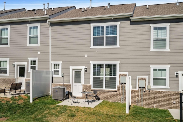 rear view of house with a yard, a patio, brick siding, and central AC