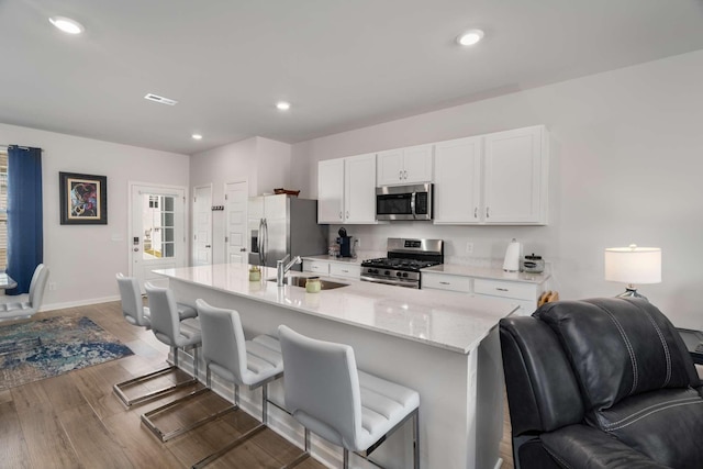 kitchen with light wood finished floors, appliances with stainless steel finishes, white cabinets, a sink, and a kitchen breakfast bar