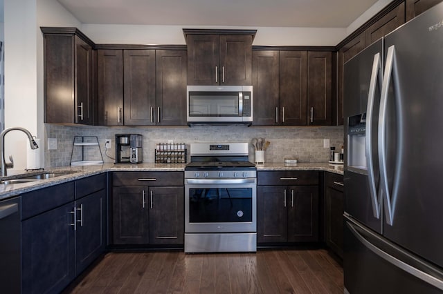 kitchen featuring dark wood finished floors, appliances with stainless steel finishes, a sink, dark brown cabinetry, and light stone countertops