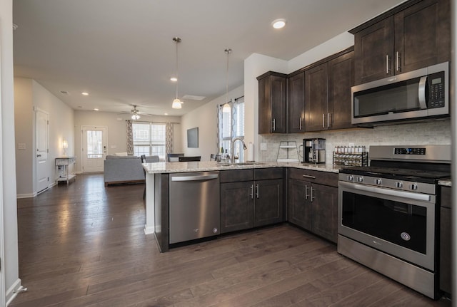 kitchen featuring a peninsula, open floor plan, appliances with stainless steel finishes, light stone countertops, and decorative light fixtures