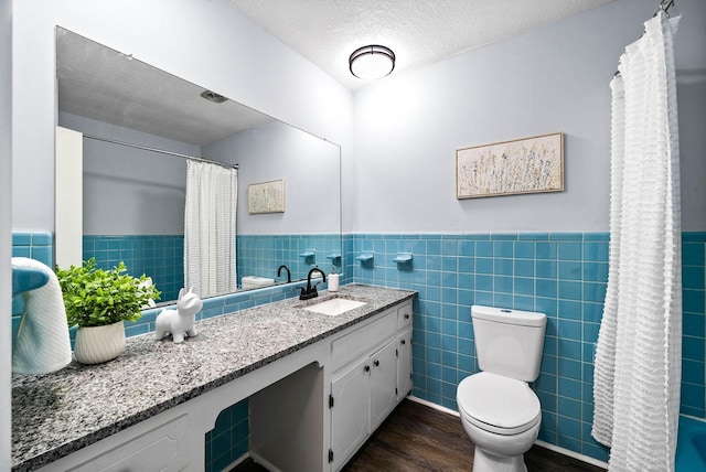 bathroom with a wainscoted wall, tile walls, vanity, a textured ceiling, and wood finished floors