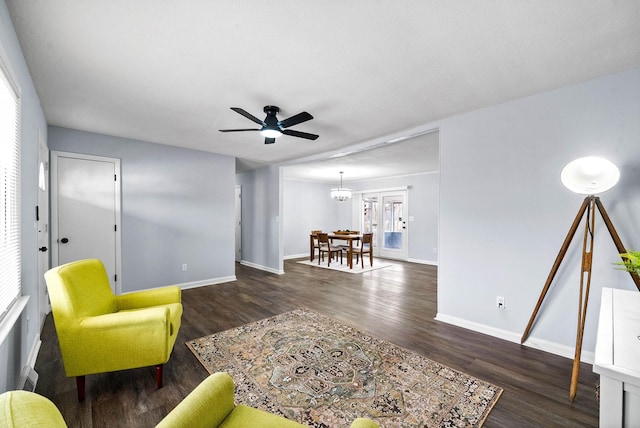 living area with ceiling fan with notable chandelier, dark wood-type flooring, and baseboards