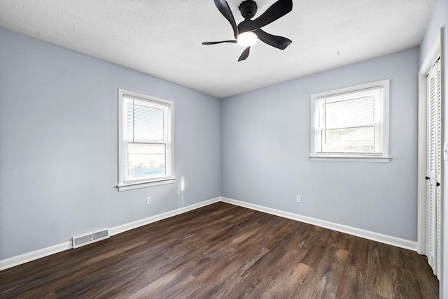 spare room with dark wood-type flooring, a healthy amount of sunlight, visible vents, and baseboards