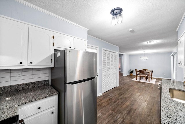 kitchen with dark stone countertops, decorative backsplash, freestanding refrigerator, and white cabinets