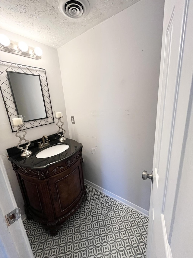 bathroom with a textured ceiling, vanity, visible vents, and baseboards