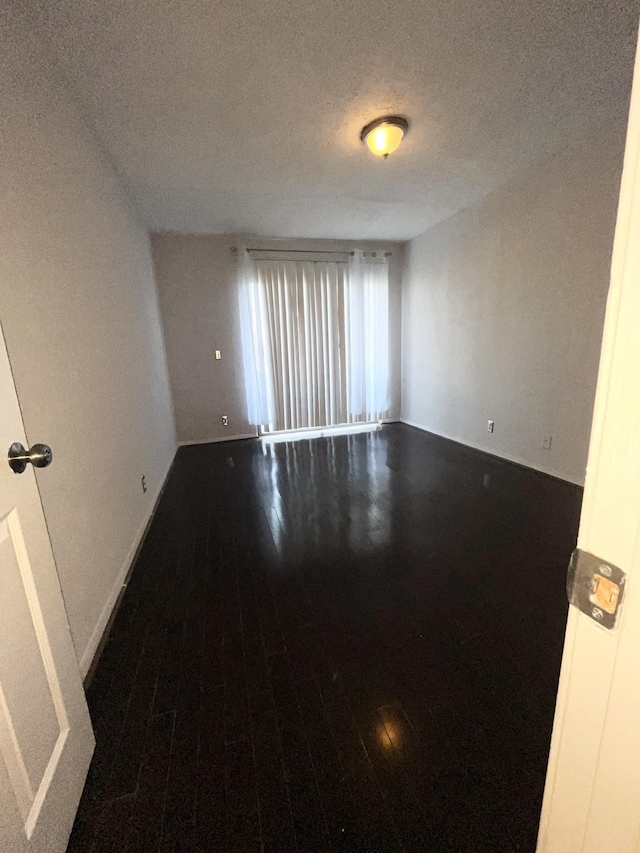 spare room featuring a textured ceiling, baseboards, and wood finished floors