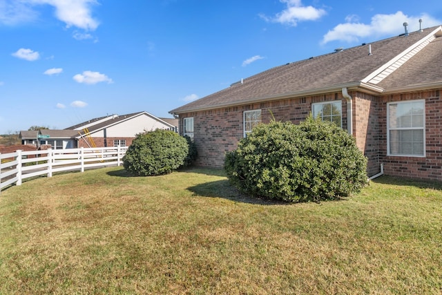 view of side of home featuring roof with shingles, fence, a lawn, and brick siding