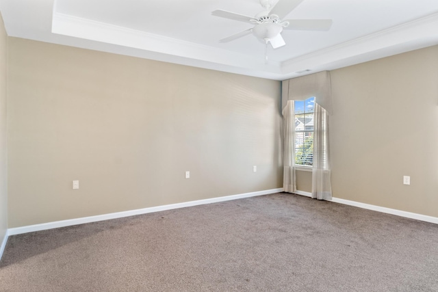 carpeted empty room featuring a raised ceiling, a ceiling fan, and baseboards