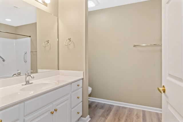 bathroom featuring toilet, wood finished floors, vanity, baseboards, and a shower