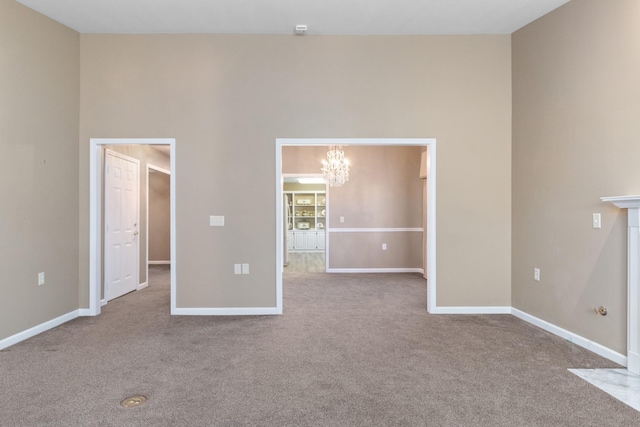 empty room with a towering ceiling, an inviting chandelier, baseboards, and light colored carpet