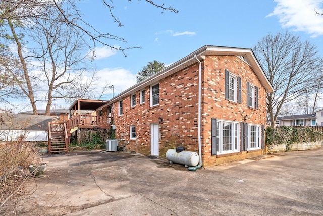 view of property exterior with a deck, central AC unit, stairway, and brick siding