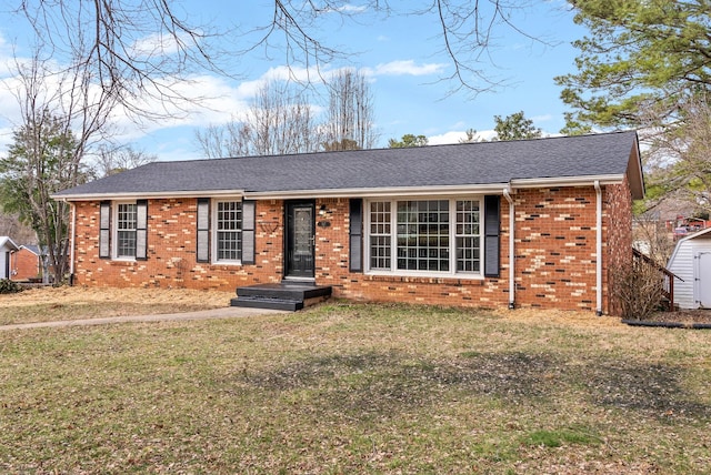 ranch-style home featuring a shingled roof, brick siding, a front lawn, and a shed