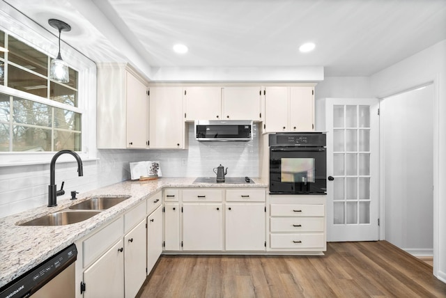 kitchen with decorative backsplash, wood finished floors, hanging light fixtures, black appliances, and a sink