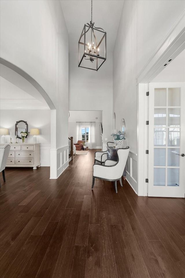 foyer featuring dark wood-style floors, arched walkways, wainscoting, and a decorative wall