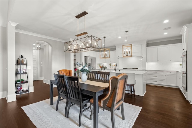 dining area with crown molding, arched walkways, dark wood-type flooring, and recessed lighting