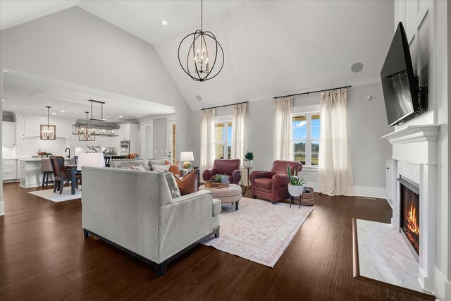 living room with dark wood-style floors, high vaulted ceiling, recessed lighting, a chandelier, and a warm lit fireplace