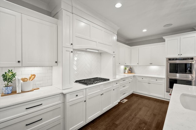 kitchen with appliances with stainless steel finishes, white cabinets, crown molding, and dark wood-type flooring