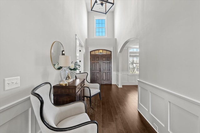 entrance foyer featuring arched walkways, a wainscoted wall, dark wood finished floors, and a decorative wall