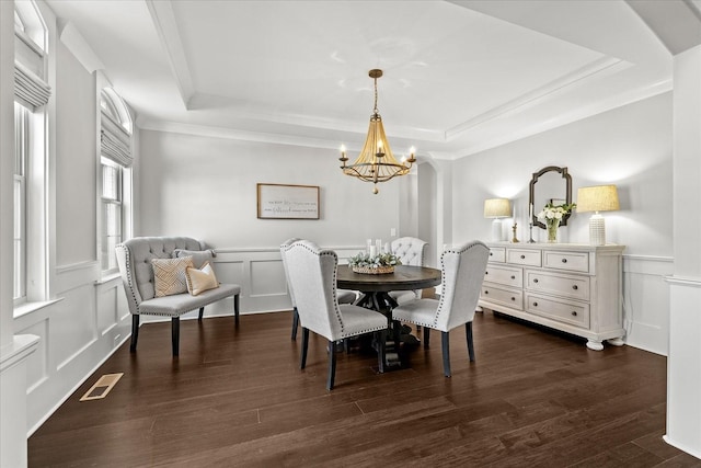 dining area with a notable chandelier, a decorative wall, visible vents, dark wood-style floors, and a raised ceiling