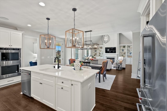 kitchen featuring an island with sink, appliances with stainless steel finishes, open floor plan, pendant lighting, and a sink