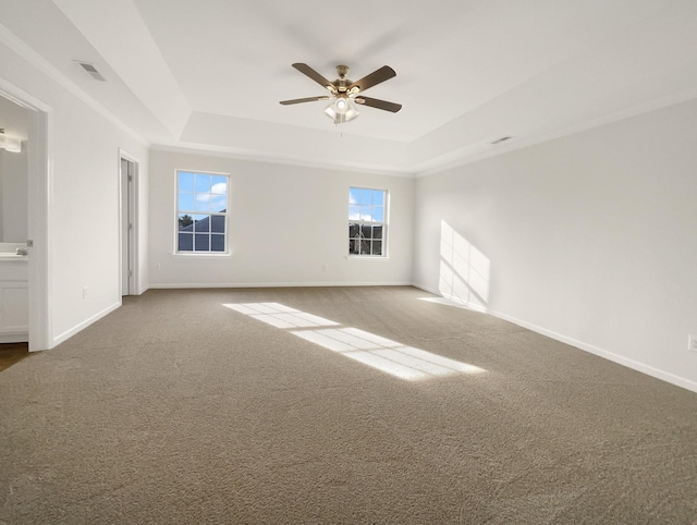 carpeted empty room with a ceiling fan, a raised ceiling, visible vents, and baseboards