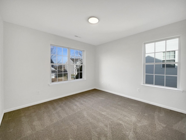 unfurnished room featuring baseboards, dark carpet, and a wealth of natural light