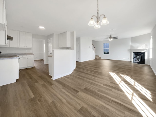 unfurnished living room featuring stairs, dark wood-type flooring, a fireplace, and baseboards