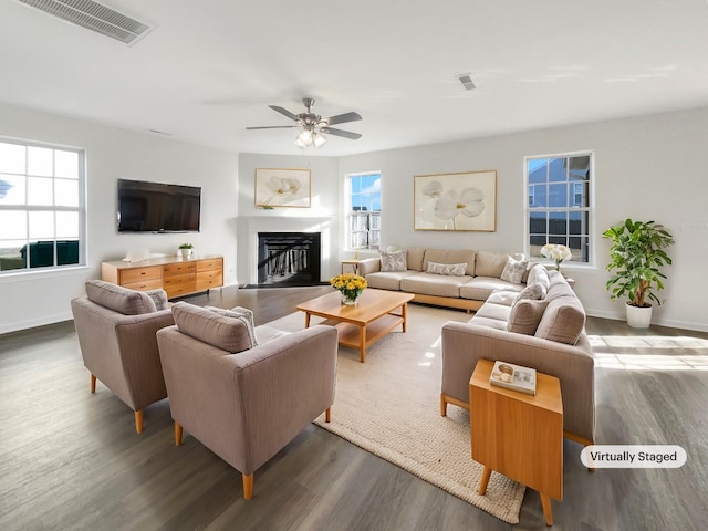 living area featuring visible vents, dark wood finished floors, a wealth of natural light, and a glass covered fireplace