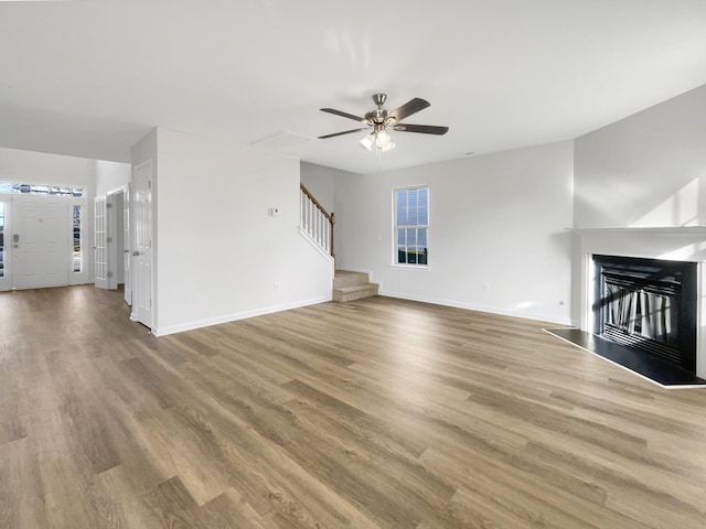 unfurnished living room featuring a glass covered fireplace, stairway, baseboards, and wood finished floors